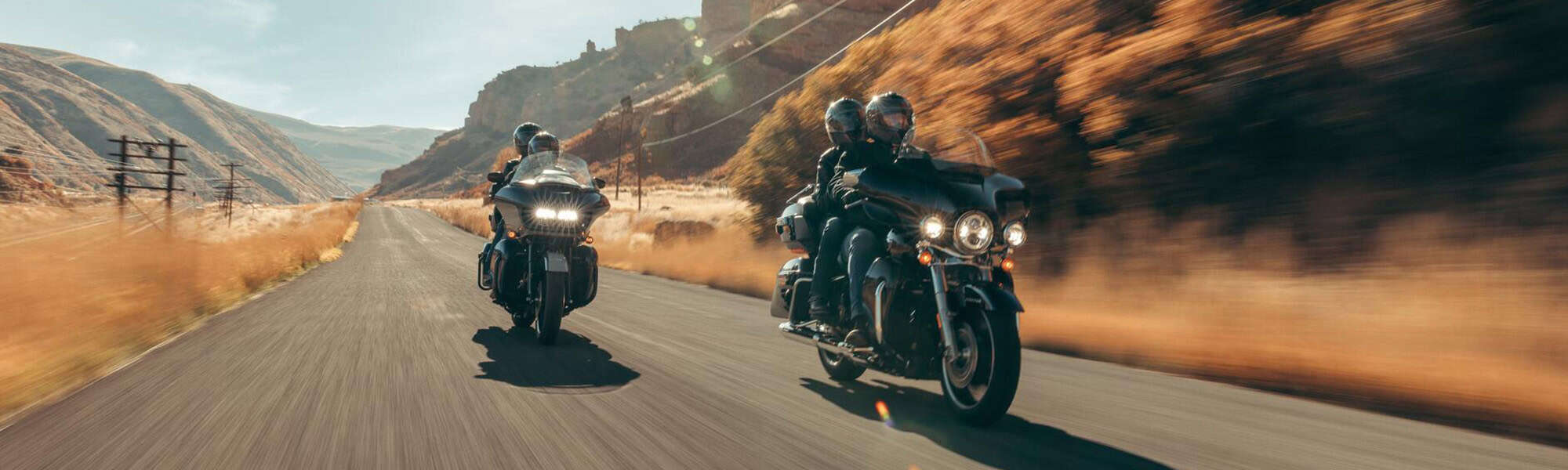 Leere Straße mit zwei Harley-Davidson Motorrädern in der Wüste, mit Bergen im Hintergrund.