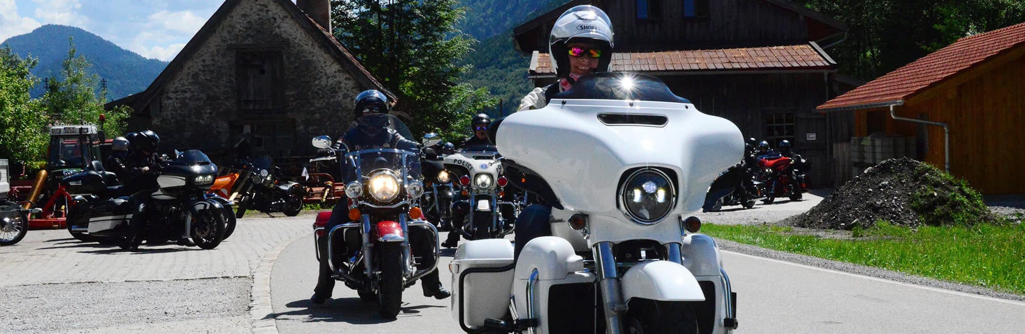 Harley-Davidson Motorräder bei Ausfahrt vor rustikalen Häusern in den Bergen.
