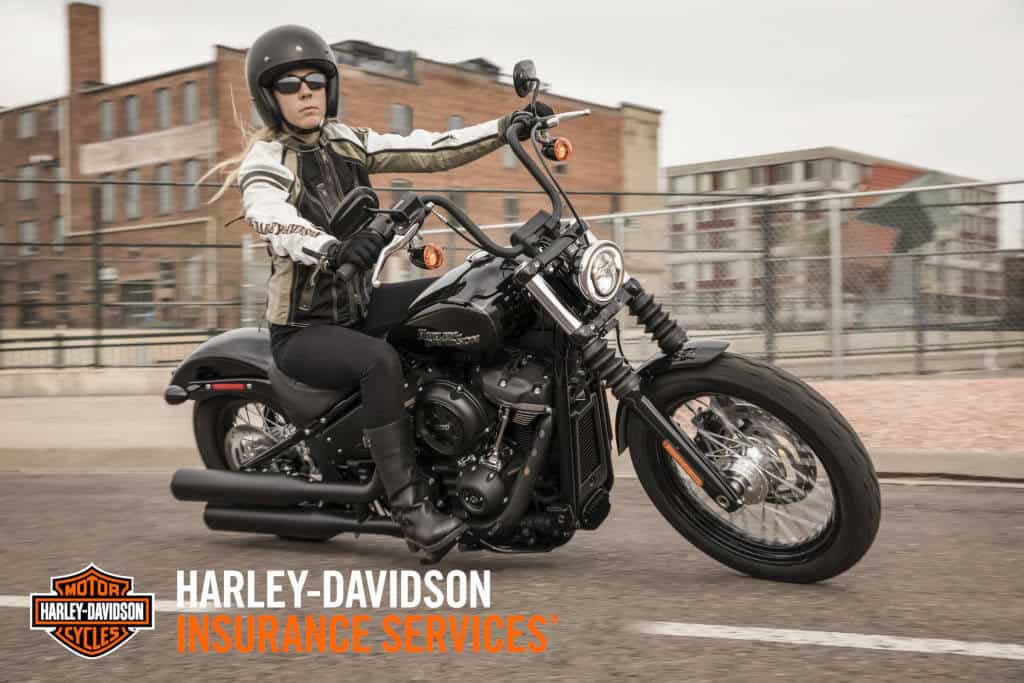 Harley-Davidson Motorradfahrerin auf schwarzer Harley; stilvoller Schutzhelm, Anzug, urbanes Ambiente.